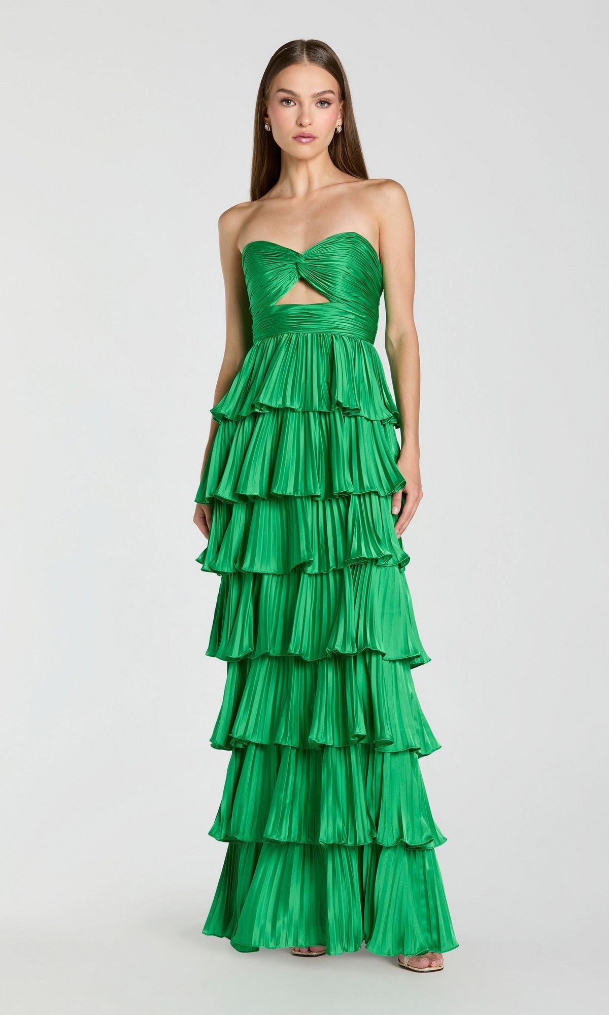 A woman in a Spring Green Mac Duggal 49981 long formal dress with a strapless pleated design, front cutout, and tiered ruffles stands against a plain light background.